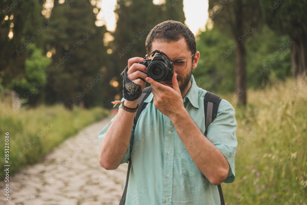 Young photographer focusing and taking a picture towards the camera in the middle of the nature Young photographer focusing and taking a picture towards the camera in the middle of the nature