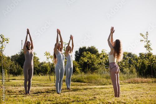 Four young women are practising yoga in the open air standing in the forest on the sunny day