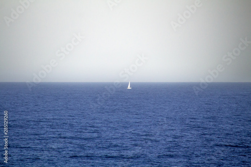 A sailing boat in a mediterranean blue sea, horizon landscape with a white sky with seagulls flying over. © Denis