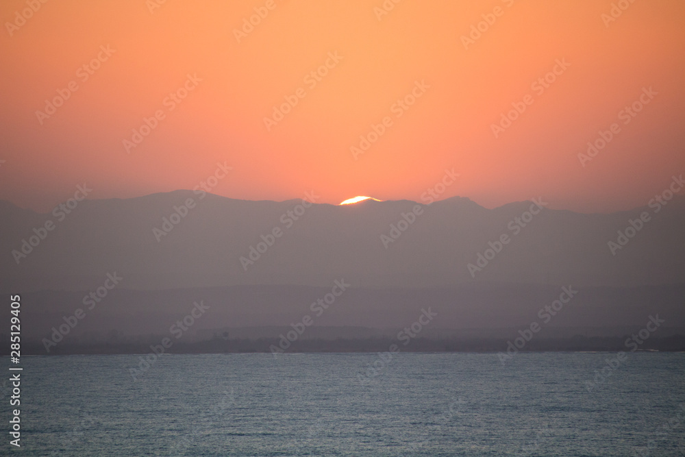 Orange sunset behind mountains and a sea in the foreground Orange sunset behind mountains and a sea in the foreground