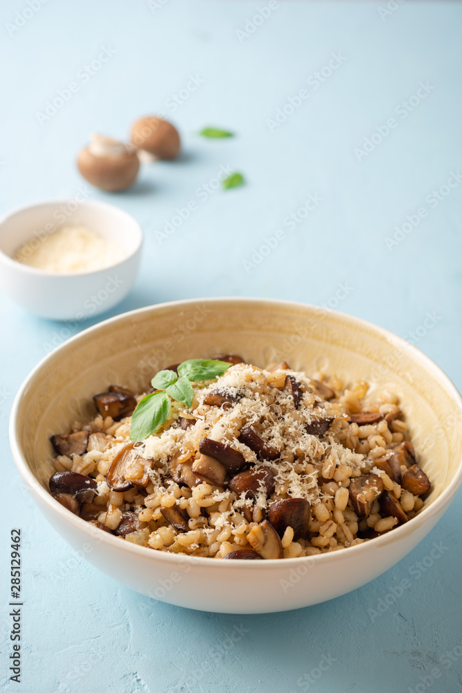 Pearl barley risotto or orzotto with mushrooms and parmesan cheese in bowl on blue concrete background. Selective focus. Pearl barley risotto or orzotto with mushrooms and parmesan cheese in bowl on blue concrete background. Selective focus.