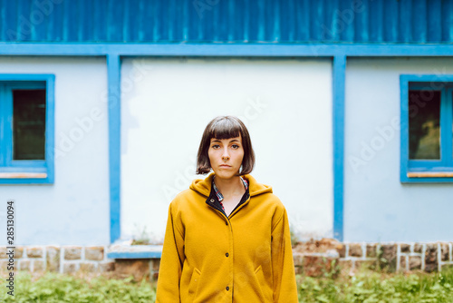 Young woman in yellow warm coat smiling and looking at camera while standing against gray wall building photo