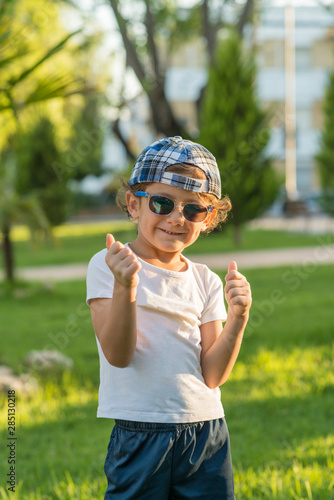 Portrait of a boy with cap and sunglasses gesturing.