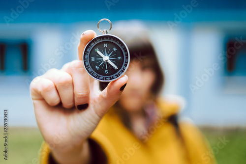 Cheerful blur young woman holding retro compass near face while standing on blurred background of countryside house photo