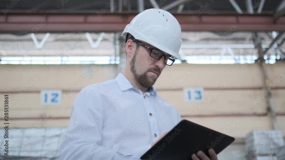 Worker male warehouse worker engineer man in a helmet working on the construction site of the warehouse, tablet computer, checking the warehouse, inspection of goods Worker male warehouse worker engineer man in a helmet working on the construction site of the warehouse, tablet computer, checking the warehouse, inspection of goods