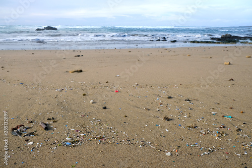 Beach polluted with microplastics, ocean waves in blurred background.