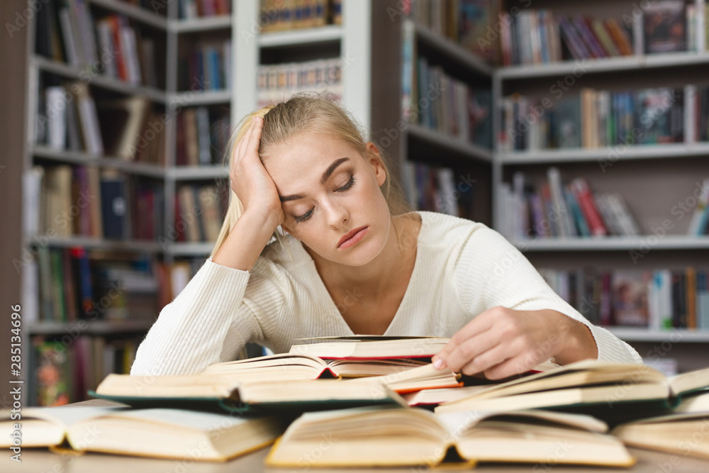 Fatigued blondy girl reading book in library Fatigued blondy girl reading book in library
