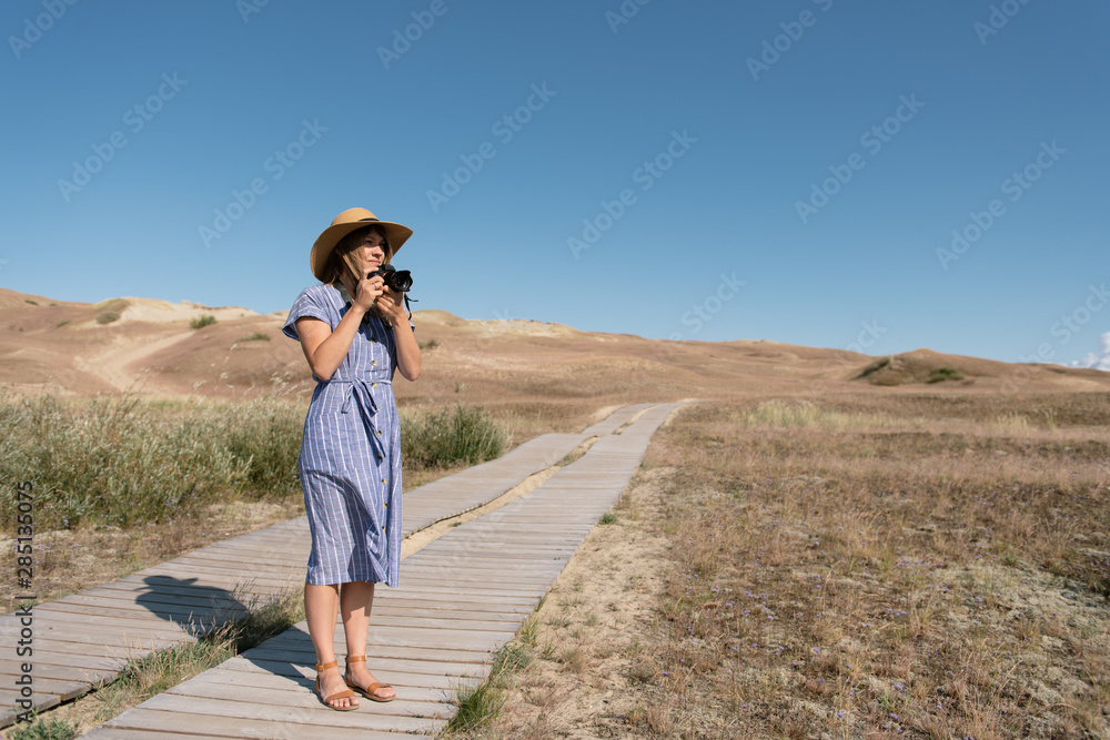 adult woman in straw hat and dress with camera standing on country path adult woman in straw hat and dress with camera standing on country path