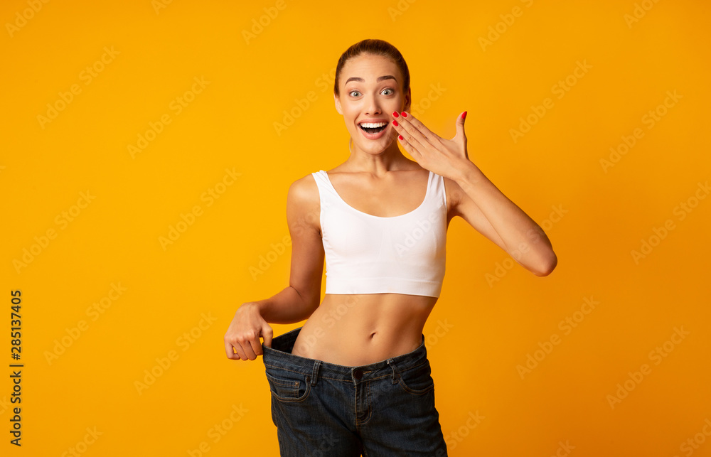 Excited Girl Posing In Oversize Jeans Over Yellow Studio Background - obrazy, fototapety, plakaty 