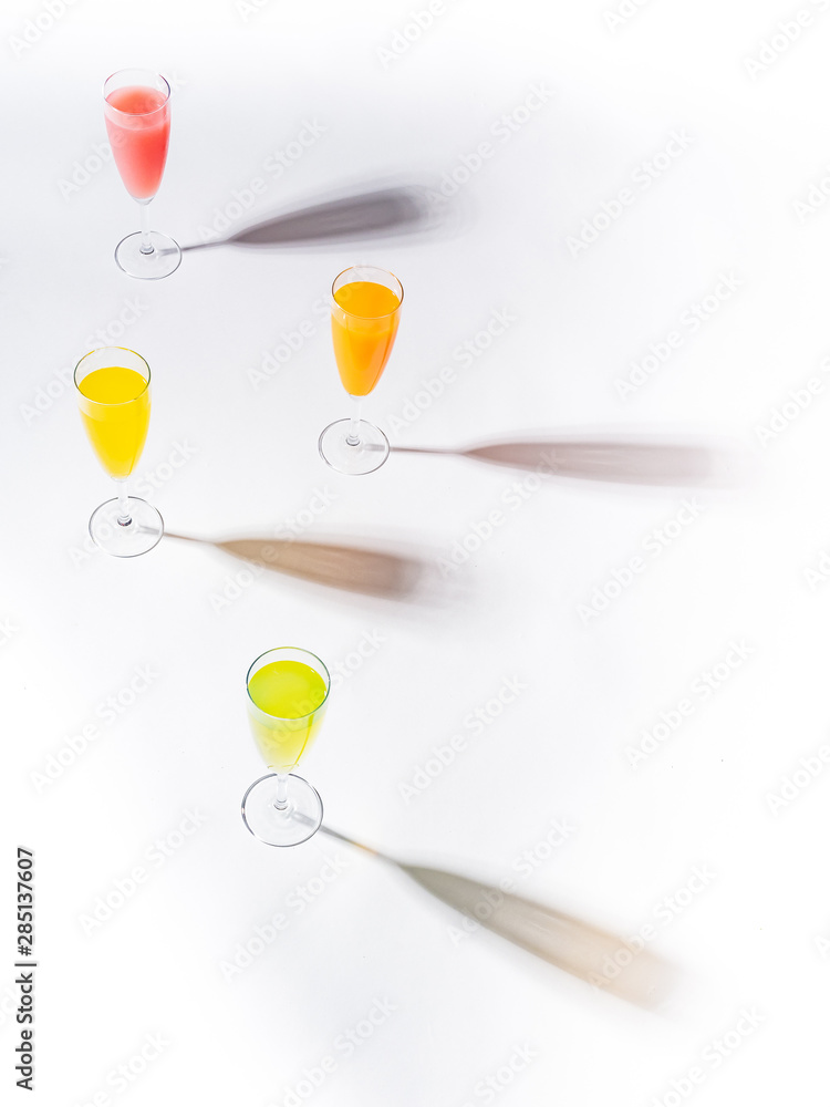 Contrasting shadows from glasses of juicy appetizing orange red yellow green drinks on white background Contrasting shadows from glasses of juicy appetizing orange red yellow green drinks on white background