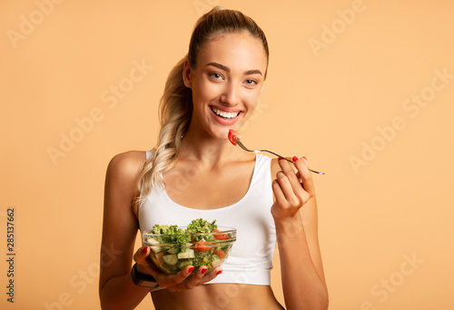 Fototapete Fit Woman Eating Fresh Salad Over Pink Studio Background