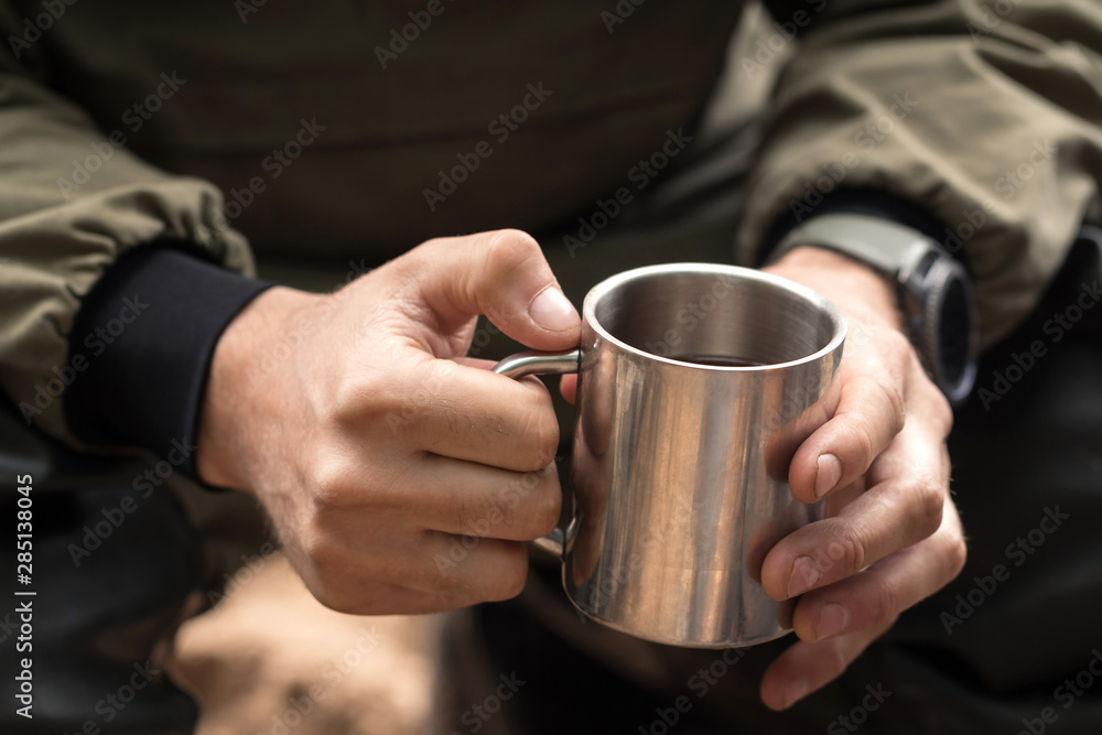 Concept adventure or tourism. Man traveler hands holding cup of hot drink outdoors. Coffee cooked over a campfire. Hiker drinking tea from mug. Bonfire on nature in wild forest Concept adventure or tourism. Man traveler hands holding cup of hot drink outdoors. Coffee cooked over a campfire. Hiker drinking tea from mug. Bonfire on nature in wild forest