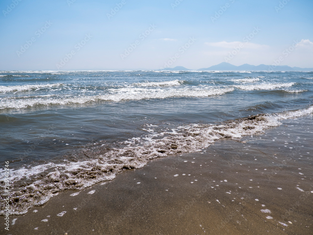 Sea with waves. Sandy beach. Horizon and mountains.