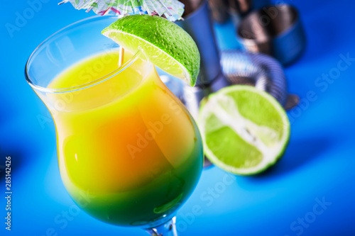 Double layer green yellow alcoholic cocktail with mango juice, rum, liqueur, lime and ice, blue background, copy cpase photo