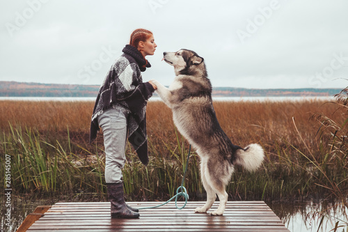 redhaired caucasian woman owner with her malamute grey big dog near the lake
