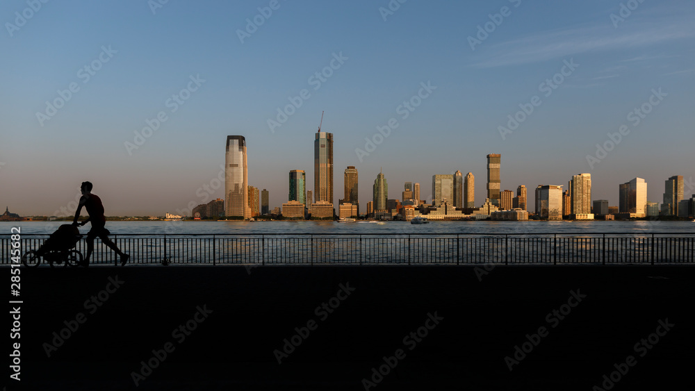 Jersey city view from Hudson pier ,shadow of running man with stroller Jersey city view from Hudson pier ,shadow of running man with stroller