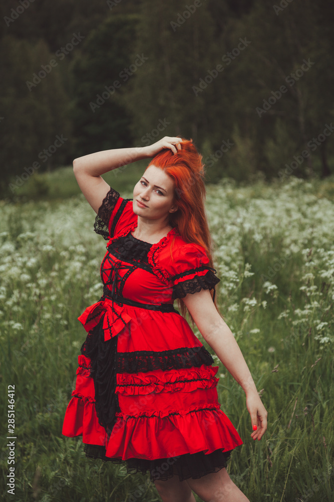 pretty redheaded woman in Little Red fairytale dress in the grass meadow