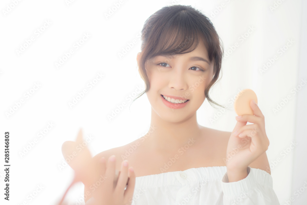 Portrait beautiful young asian woman applying powder puff at cheek makeup of cosmetic looking mirror, beauty of girl with skin face smile in the bedroom, health and wellness concept. Portrait beautiful young asian woman applying powder puff at cheek makeup of cosmetic looking mirror, beauty of girl with skin face smile in the bedroom, health and wellness concept.