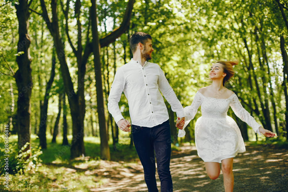 A beautiful and gentle girl with light hair and a white dress is walking in a sunny summer forest with her handsome guy in a white shirt and dark pants and they playing with cute gray dog A beautiful and gentle girl with light hair and a white dress is walking in a sunny summer forest with her handsome guy in a white shirt and dark pants and they playing with cute gray dog