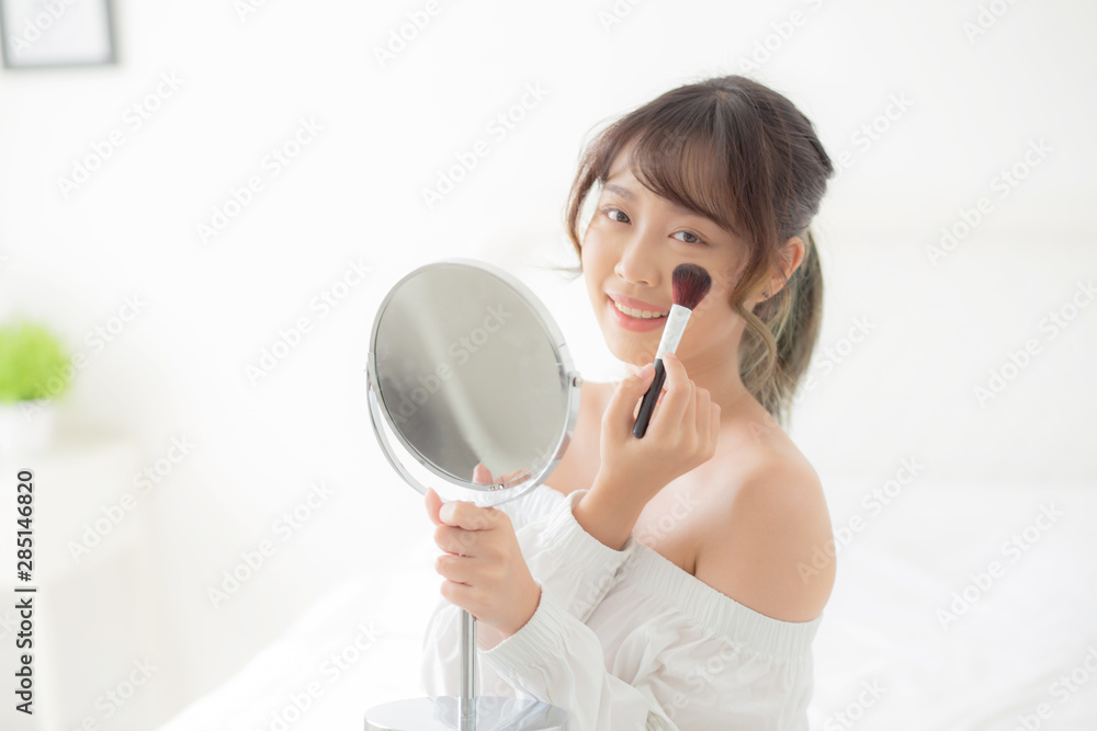 Beauty portrait young asian woman smile with face looking mirror applying makeup with brush cheek in the bedroom, beautiful of girl holding blusher, skin care and cosmetic concept. Beauty portrait young asian woman smile with face looking mirror applying makeup with brush cheek in the bedroom, beautiful of girl holding blusher, skin care and cosmetic concept.