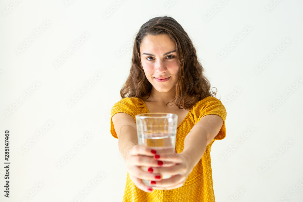 Close-up of one beautiful girl with smile, long hair and red-painted nails holding glass cup with water on light wall background. Health, healthy life, refresh and happiness concept. Close-up of one beautiful girl with smile, long hair and red-painted nails holding glass cup with water on light wall background. Health, healthy life, refresh and happiness concept.
