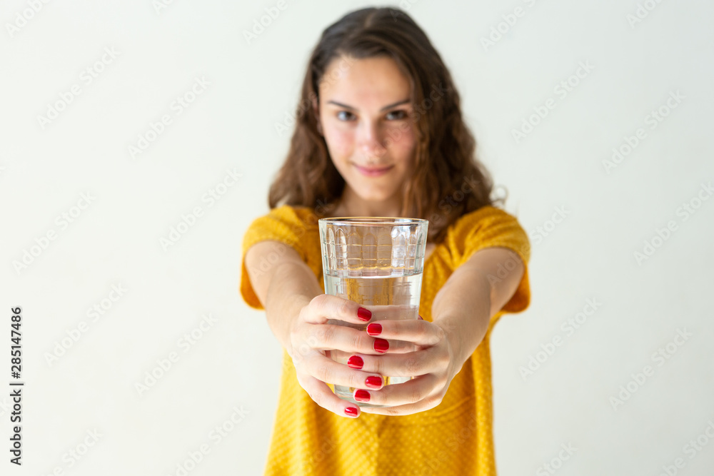 Close-up of one beautiful girl with smile, long hair and red-painted nails holding glass cup with water on light wall background. Health, healthy life, refresh and happiness concept. Close-up of one beautiful girl with smile, long hair and red-painted nails holding glass cup with water on light wall background. Health, healthy life, refresh and happiness concept.