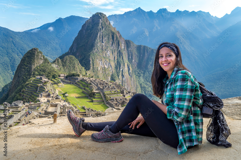 A woman sitting on a Machu Picchu terrace. You can see the ruins of the citadel of Machu Picchu, the Huayna Picchu mountain and other huge mountains behind. Archaeological site, UNESCO World Heritage A woman sitting on a Machu Picchu terrace. You can see the ruins of the citadel of Machu Picchu, the Huayna Picchu mountain and other huge mountains behind. Archaeological site, UNESCO World Heritage