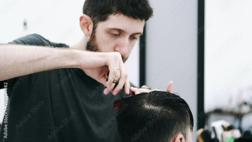 attractive businessman sitting in a chair while getting a modern and stylish haircut from a barber at the hair salon attractive businessman sitting in a chair while getting a modern and stylish haircut from a barber at the hair salon
