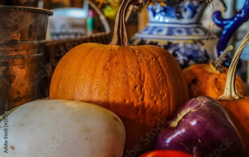 Autumn vegetable arrangement on a wooden table in a farmhouse keeping room  selective focus on foreground  including pumpkin purple bell peppers white eggplant orange and red
