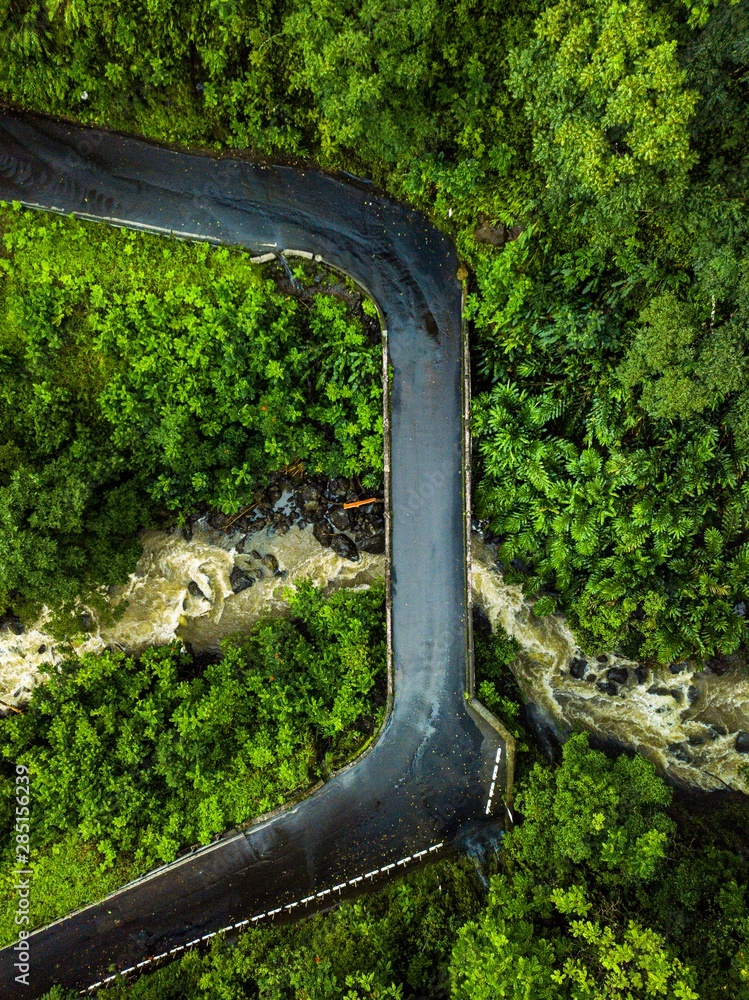 A drone aerial birds eye view, one of many old vintage bridges and the Road to Hana. Waterfalls in the background create a powerful river of water on the beautiful island of Maui, Hawaii.