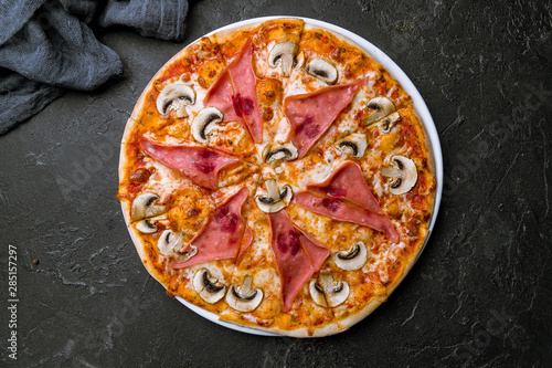 Pizza with ham and mushrooms on black concrete table