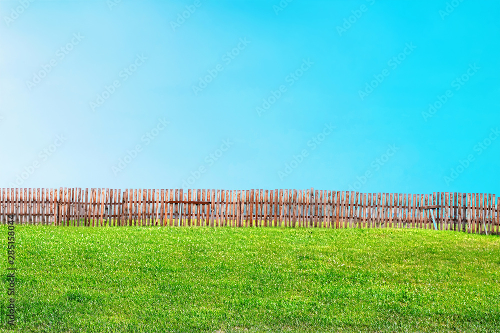 landscape of green lawn and blue sky divided in half by fence