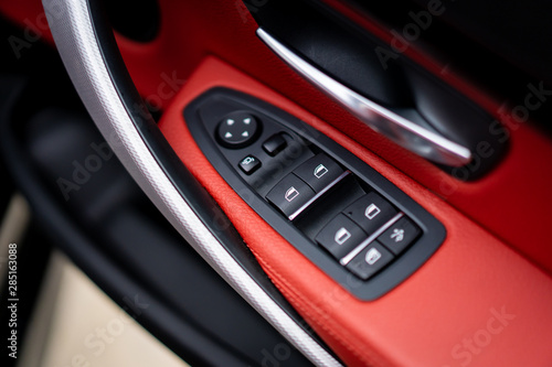 Windows and lock controller in the modern luxury car covered by beautiful red leather close up. © DG PhotoStock