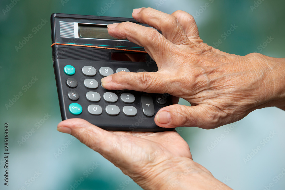 Senior woman's hands holding old calculator in bokeh blue swimming pool background, Close up shot, Selective focus, Business concept Senior woman's hands holding old calculator in bokeh blue swimming pool background, Close up shot, Selective focus, Business concept