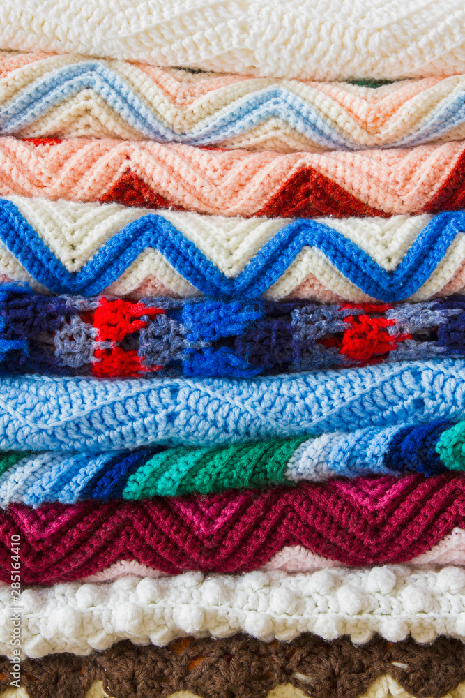 A colorful stack of folded crochet afghans; cozy, handmade crochet blankets in a pile A colorful stack of folded crochet afghans; cozy, handmade crochet blankets in a pile