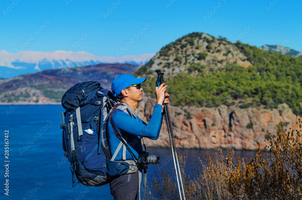 Man with trekking poles and backpack taking picture on a mountain trail above the sea