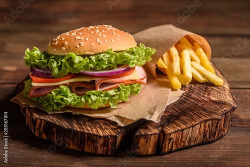 Tasty grilled homemade burger with beef, tomato, cheese, cucumber and lettuce. Delicious grilled burgers. Craft beef burger and french fries on wooden table.