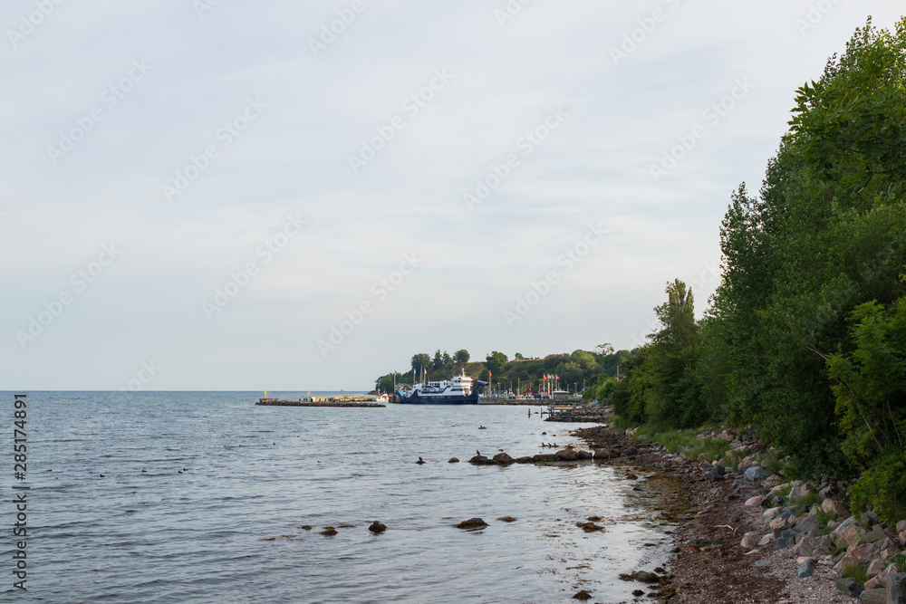 A stone beach on the island of Ven in southern Sweden with the ferry Stjernborg visible while stopping in the harbor of Bäckviken during a summer sunset. 