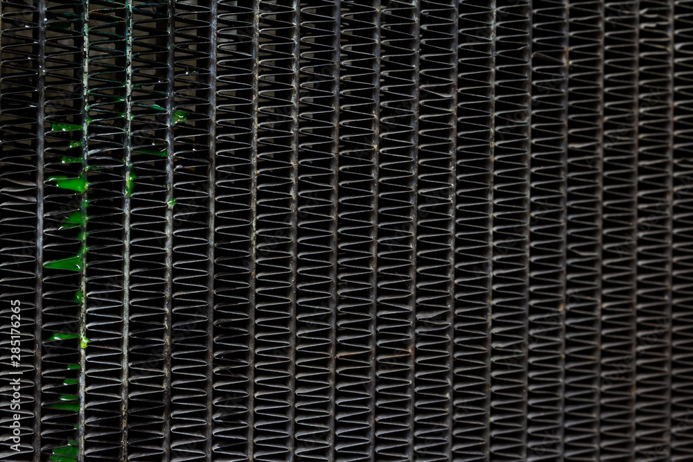 Close up textured and fins with group of fresh green coolant liquid leaked out of the old aluminum car radiator waiting for repair background. Selective focus and copy space.