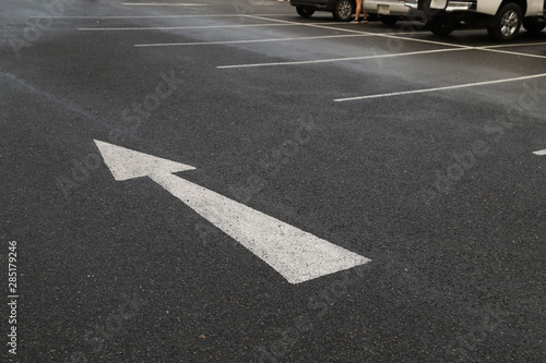 Closeup of arrow sign on asphalt ground of the parking lot after raining.  © Amphon