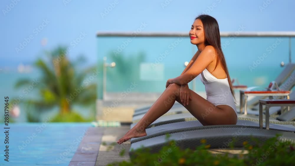 Beautiful asian woman relaxes at swimming pool in a white swim suit.