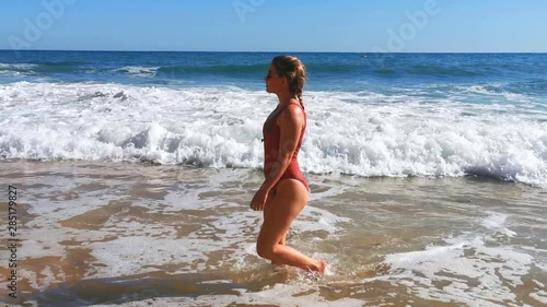 Girl in a swimsuit, walking in the water,trying to swim between big waves, at the Praia dos Caneiros beach, at the Atlantic sea, on a sunny summer day, on the coast of Lagos, Algarve, Portugal