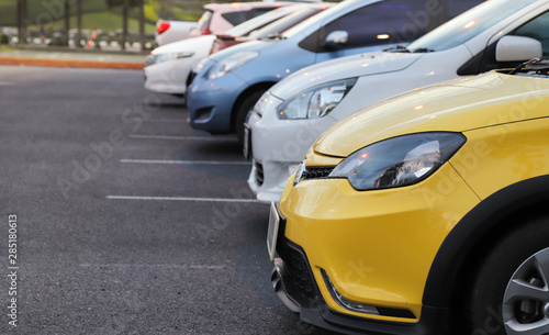 Closeup of front side of yellow car and other cars parking in parking area after raining. 