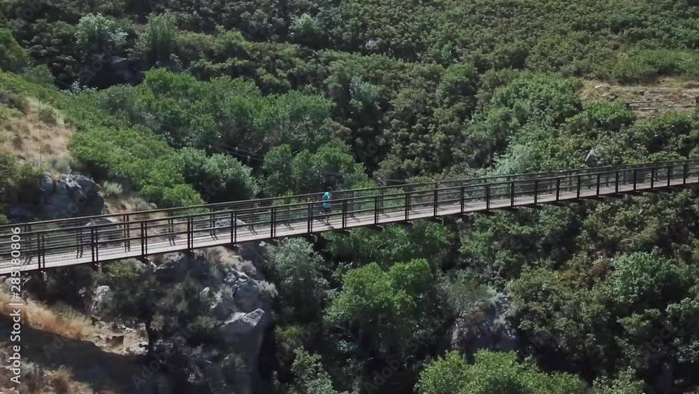 Drone Shot following an active man running on an outdoor hanging suspension bridge above Bear Canyon in Draper City, Utah. Drone Shot following an active man running on an outdoor hanging suspension bridge above Bear Canyon in Draper City, Utah.