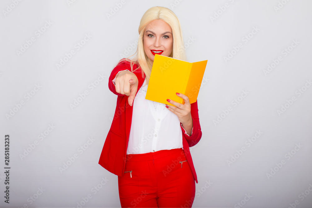 Attractive blonde haired woman wearing red jacket and pants, holding book in her hands Attractive blonde haired woman wearing red jacket and pants, holding book in her hands