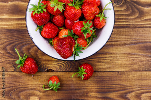 Fresh ripe strawberry in white bowl on a wooden table. Top view