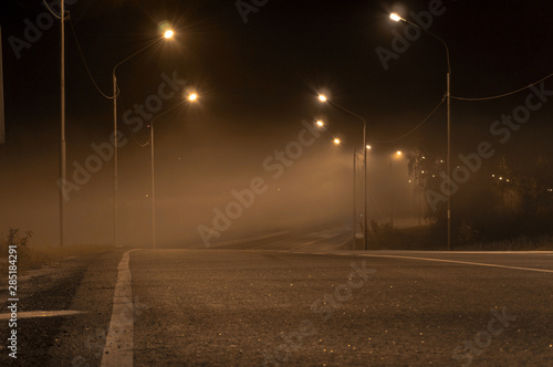 foggy night road,dim yellow light of street lamps.asphalt road. city night landscape