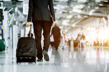 Elegant asian businessman checking email on mobile phone while walking with suitcase inside airport, experienced male employer using cell telephone while waiting for taxi car coming before work travel