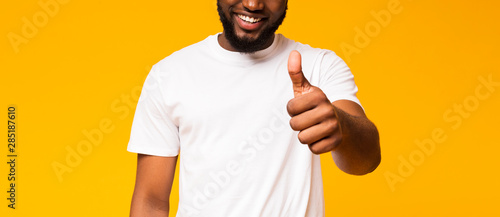 Pleased man showing thumb up, smiling broadly over yellow background
