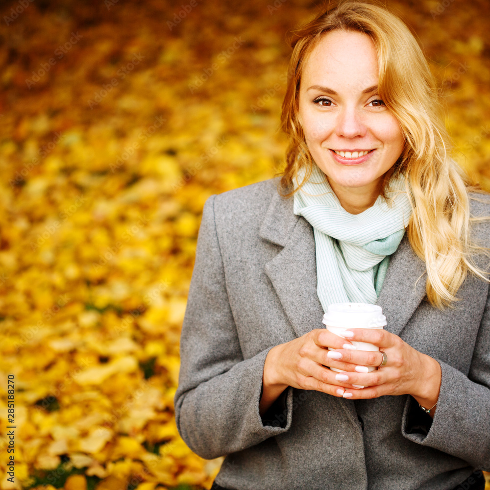 Cheerful pretty woman drinking coffee in autumn park